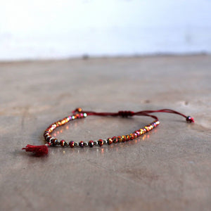 Threaded bracelet with cut glass beads featuring fine, mini tassel. Great for stacking or individual wearing. Slide-knot adjustable closure provides sizing flexibility. Shiraz.