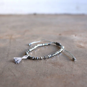 Threaded bracelet with cut glass beads featuring fine, mini tassel. Great for stacking or individual wearing. Slide-knot adjustable closure provides sizing flexibility. Silver.
