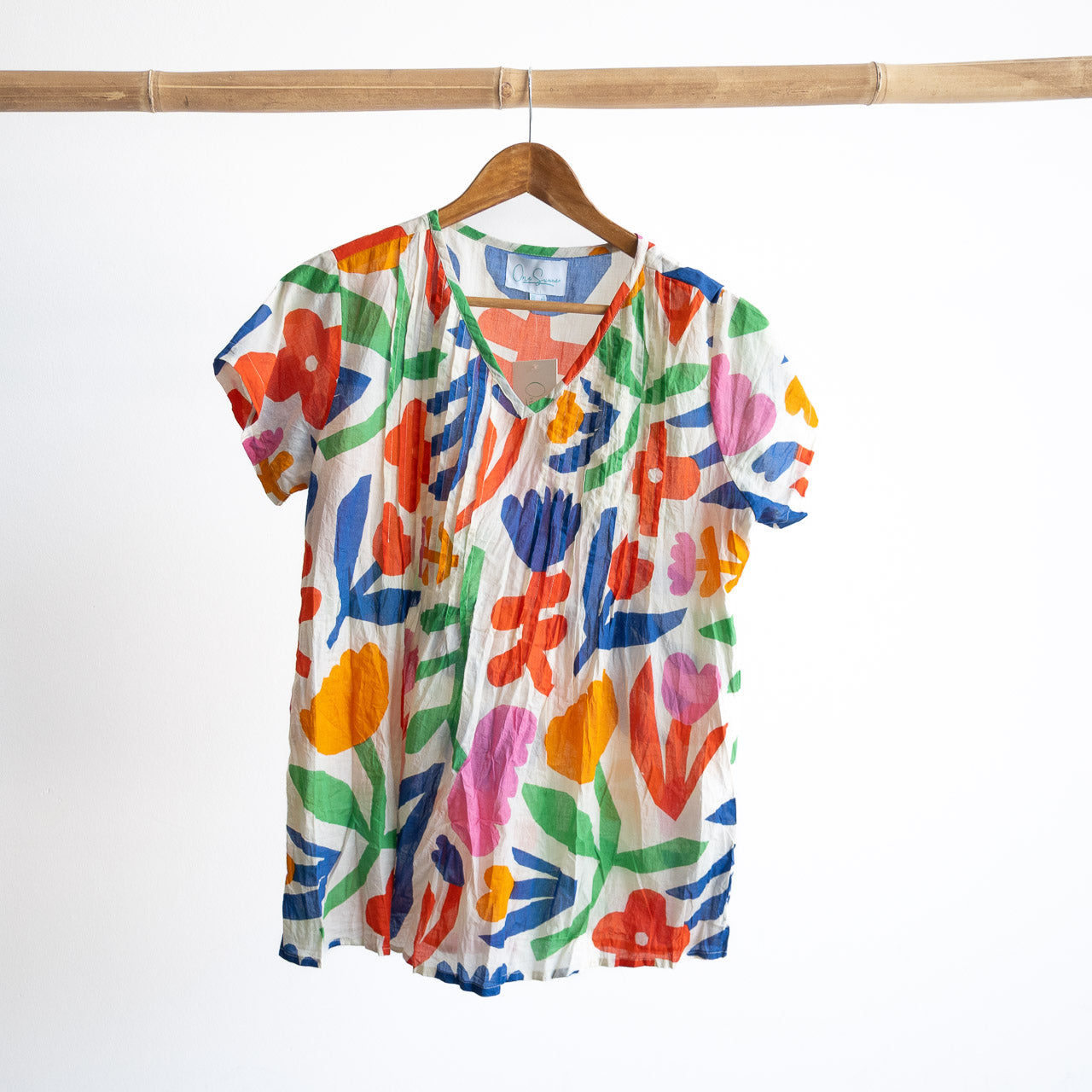 A colorful light cotton pintuck floral blouse on a hanger