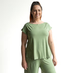 A woman with long brown hair in a ponytail, smiling, wears the Curve Hem T-Shirt by KOBOMO Bamboo with matching pants against a plain white background.