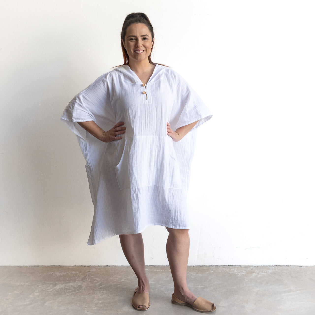 The Noosa Beach Hoodie in white cotton, an oversized poncho dress with short sleeves and a relaxed fit, paired with tan slip-ons.