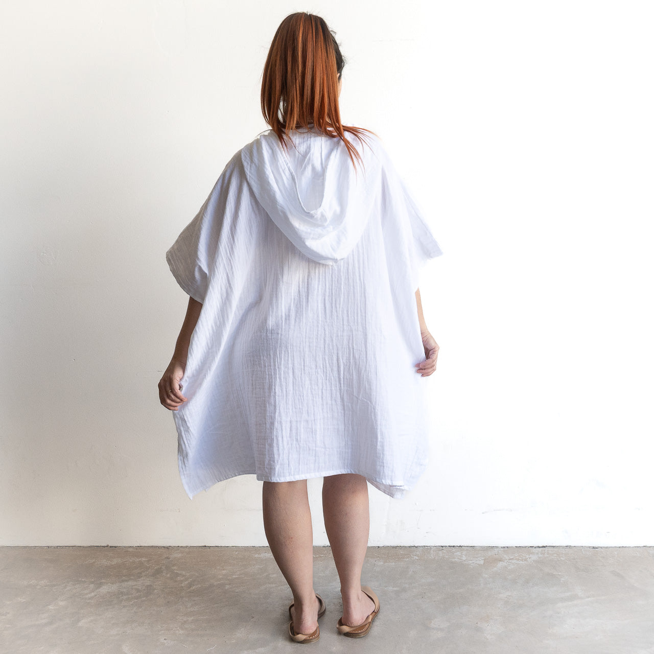 The Noosa Beach Hoodie is a loose, knee-length white cotton poncho with wide sleeves and a relaxed silhouette.