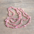 Stunning luxe-length, hand-knotted necklace made with faceted glass beads in a rainbow metallic finish. Champagne Pink.