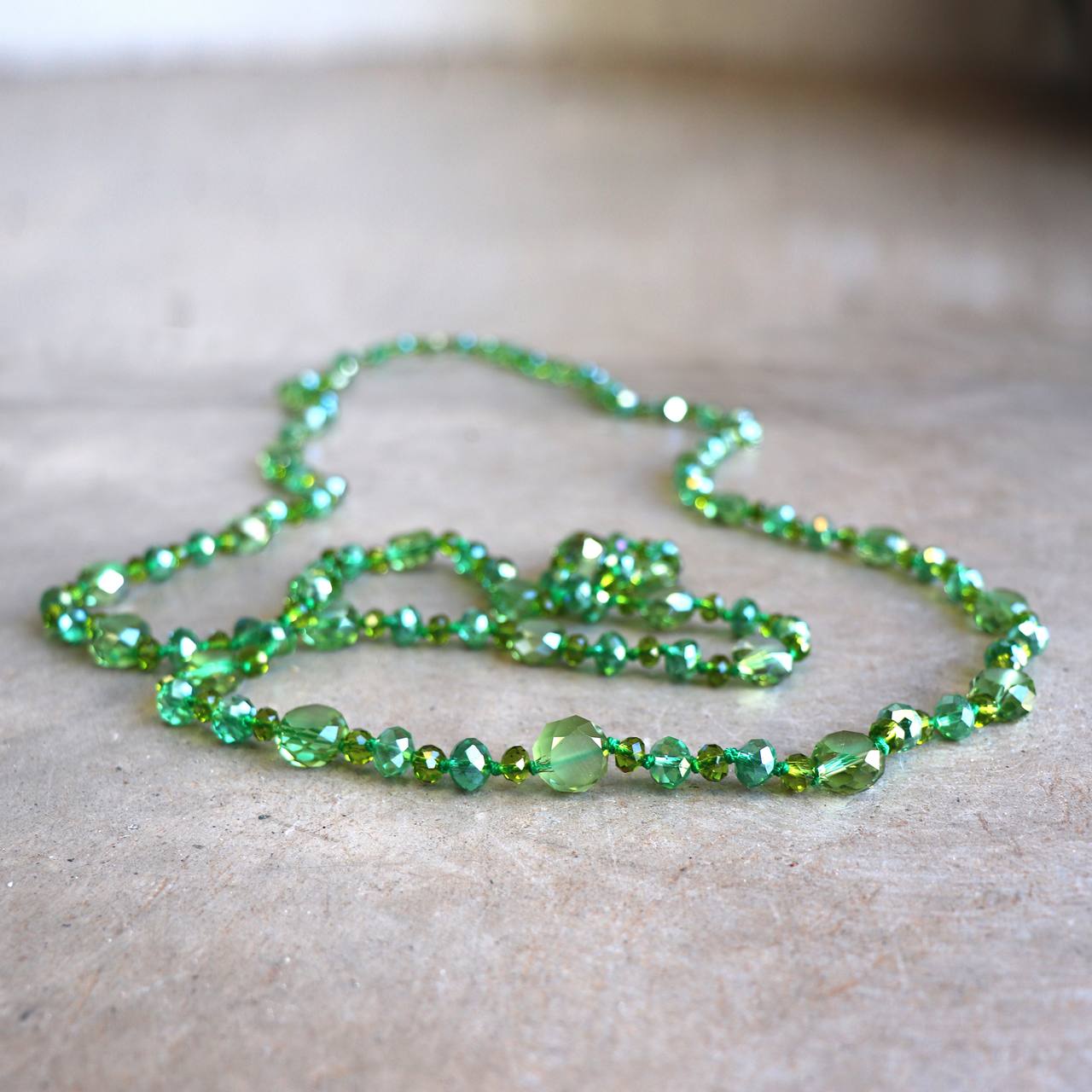 Stunning luxe-length, hand-knotted necklace made with faceted glass beads in a rainbow metallic finish. Ocean Green.