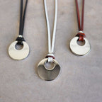 Silver Moon-shaped pendant combined with a natural leather band, available in 3 colours, Black, Silver and Tan.