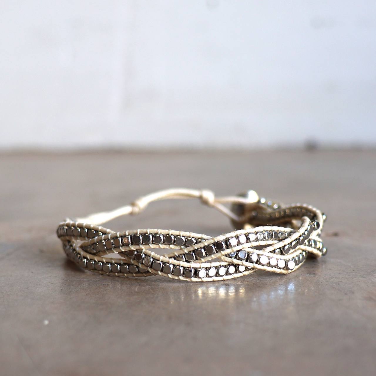 Three-strand, hand-knotted, metallic bead bracelet. Button style closure with 3 size options. Natural/Silver.