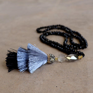 Zeta Necklace is handknotted with cut glass beads and features a tiered tassel pendant in smokey greys.